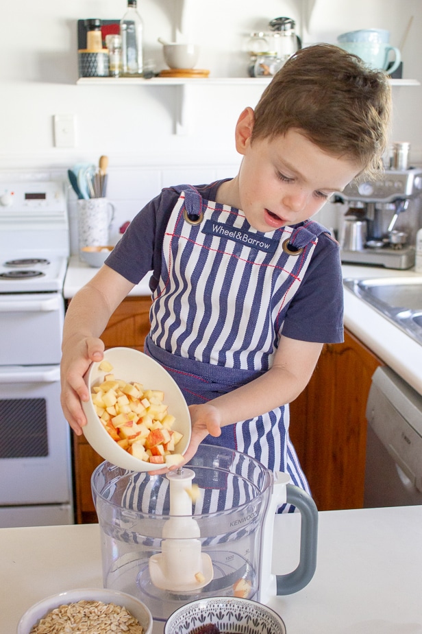 A picture of a child helping to make Apple Pie Bliss Bites by adding apple to the food processor bowl