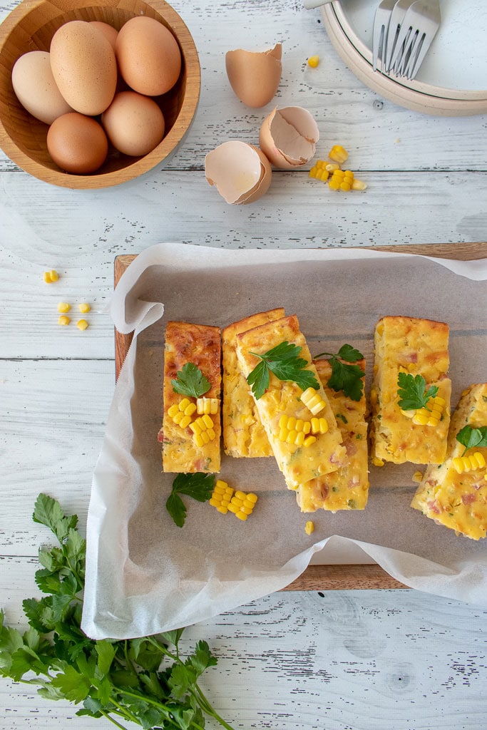 Image of corn slice with parsley, eggs and plates with forks staked on top.