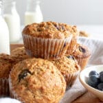 Image of baked Bran Muffins with a bowl of blueberries. In the background there are milk bottles.